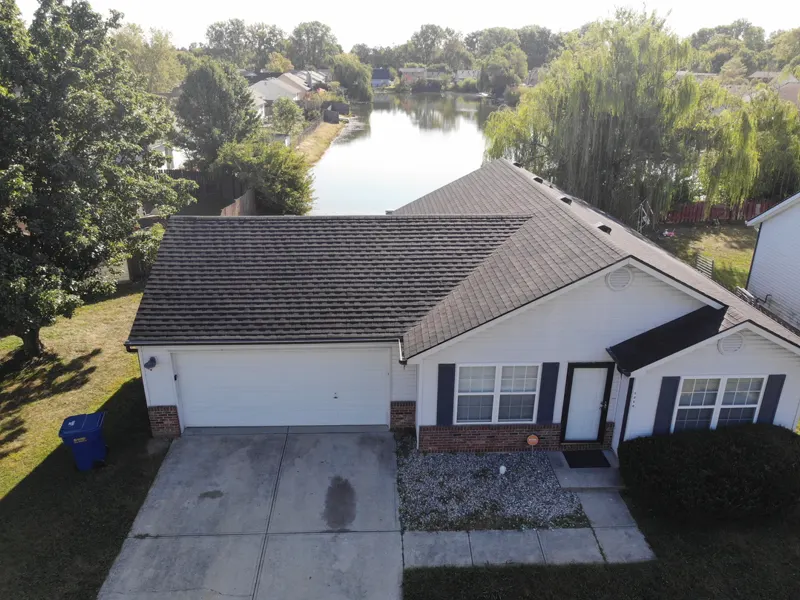 Drone photo of a finished shingle roof on a ranch home beside a neighborhood pond