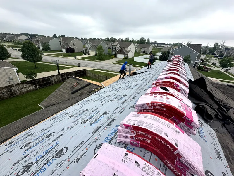 Shingle bundles staged along a ridge during a storm damage roof replacement in a Johnson County subdivision