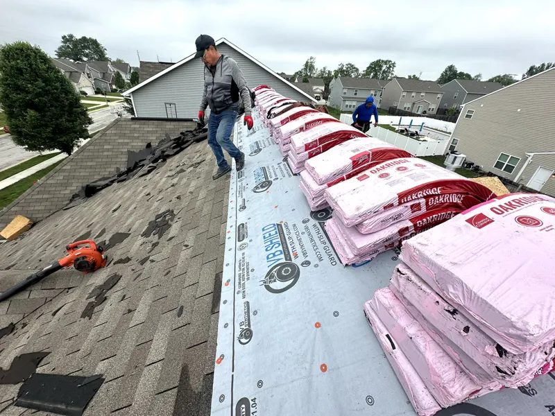 Shingle bundles staged on underlayment with crew working on a Greenwood roof